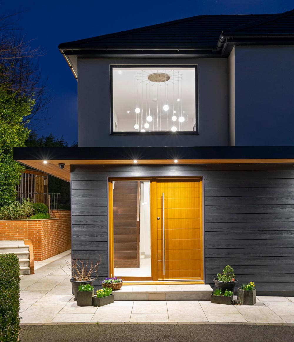 Exterior night shot of the front of a house lit with led lights and featuring a timber entrance door